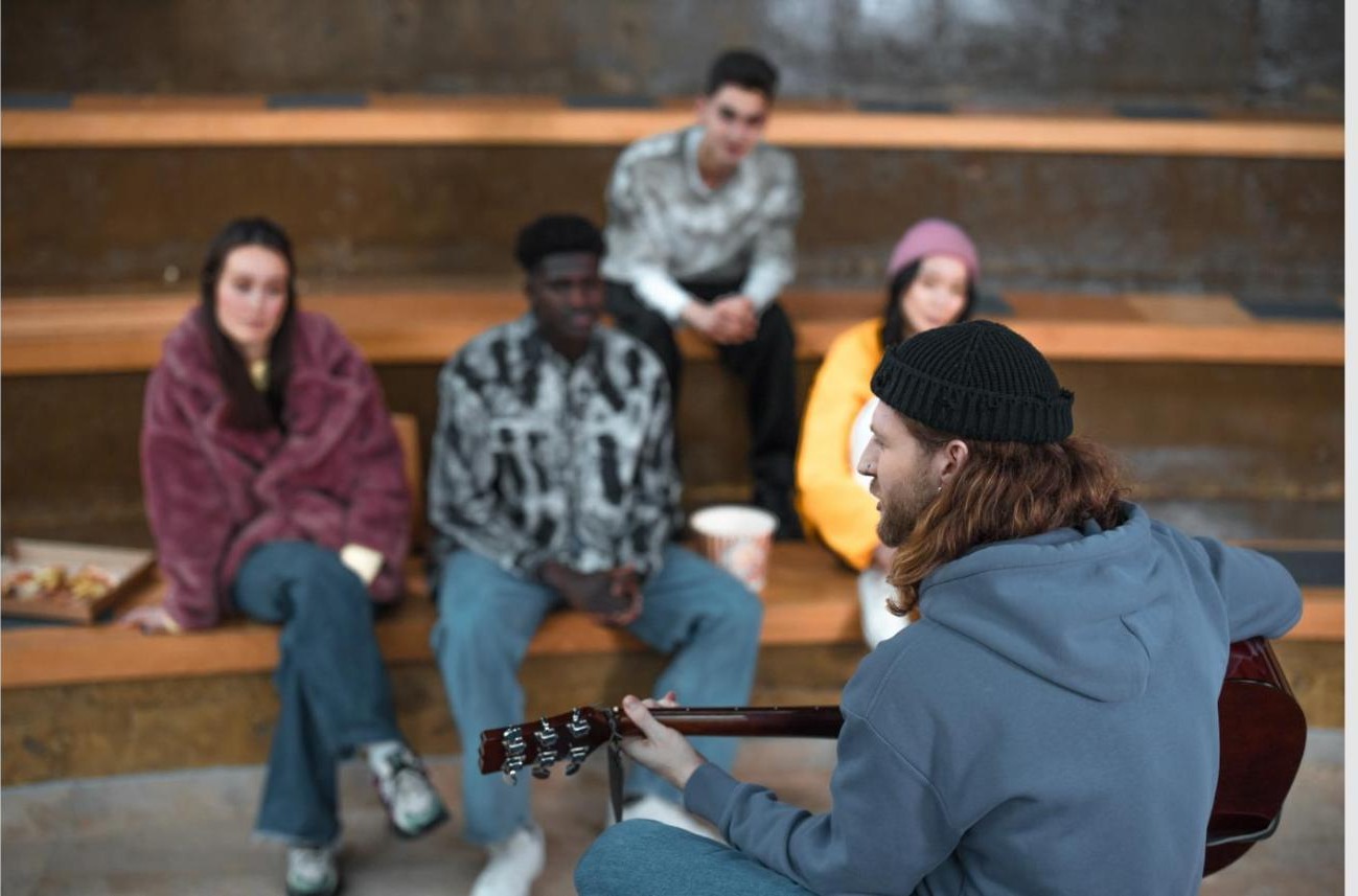 Grupo de amigos reunido ao ar livre a ouvir uma amiga a tocar guitarra